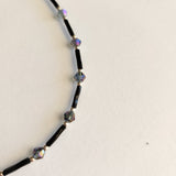 Adjustable black ankle bracelet with multicolored beads and a metallic clasp.