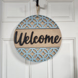 A round wooden 'Welcome' door sign with a blue oval frame and a sisal rope hanger.