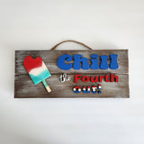 A wooden sign with a popsicle design and the text 'CHILL THE 4TH OUT' painted in blue and red colors, accompanied by a hanger.