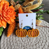 A pair of dark orange pumpkin-shaped earrings with brass hooks, displayed on a card with 'Blue Bourbon Designs' branding.