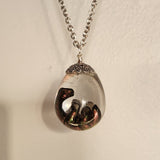 Resin dinosaur encased in clear egg pendant on stainless steel chain