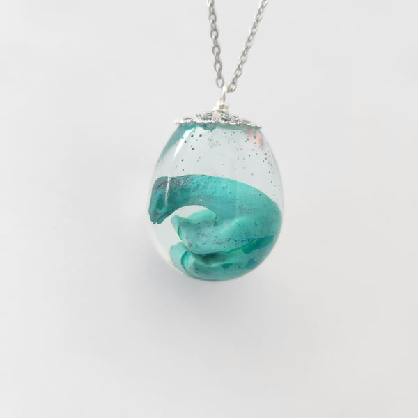 Resin dinosaur encased in clear egg pendant on stainless steel chain