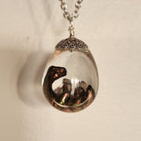Resin dinosaur encased in clear egg pendant on stainless steel chain