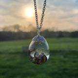 Resin dinosaur encased in clear egg pendant on stainless steel chain