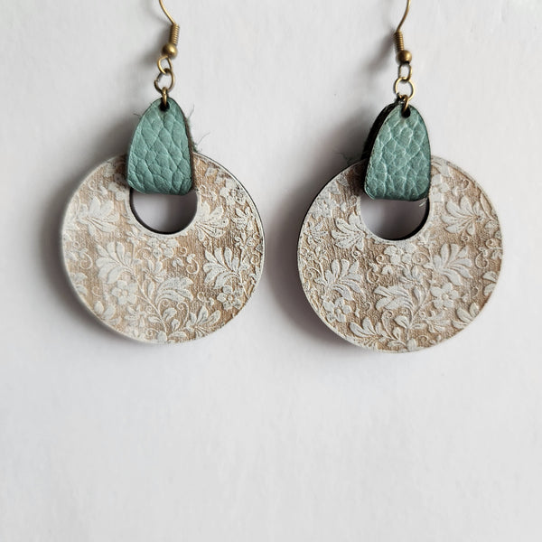 A pair of engraved wood floral circle earrings with leather accents and brass hooks.