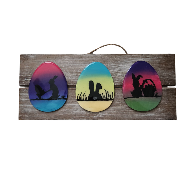 A decorative Easter egg sign featuring three hand-painted eggs on a wooden board with a rope hanger.