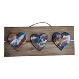 A wooden sign with three multicolored heart-shaped decorations hanging from it, each with different  patterns.