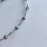 Ankle bracelet with silver tube and iridescent blue beads.