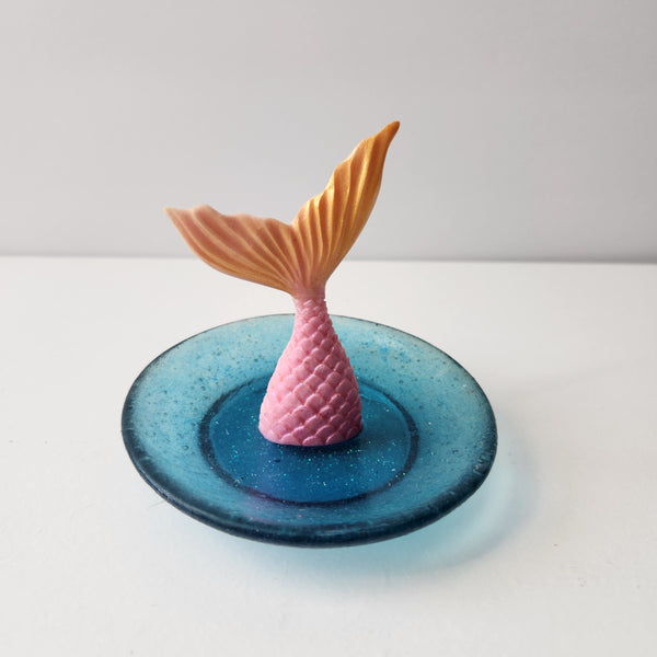 A decorative tray featuring a pink mermaid jewelry dish with a blue base and sparkles on the surface.