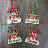 Hand painted wooden reindeer ornaments with red and green details, customized with name of your choice hanging from green and red ribbons.
