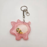 Piggybank shaker keychain filled with oil and floating charms.
