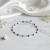 An adjustable anklet with a chain link design and purple and blue beads.