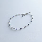 Ankle bracelet with silver tube and iridescent blue beads.