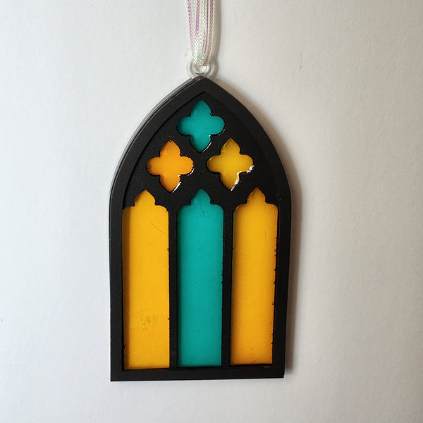 A resin stained glass window ornament with a black base and multicolored patterns, designed to look like stained glass on a ribbon hanger.