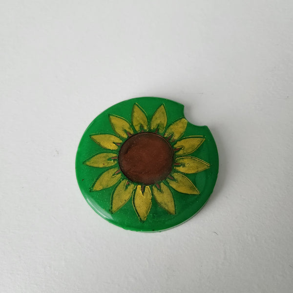 A round green car coaster with a sunflower design in the center.