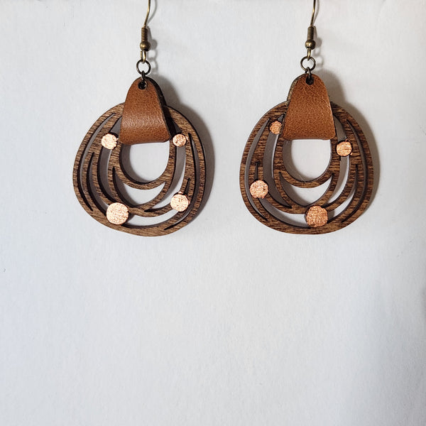 Wooden earrings with circular designs and brown leather accents on a light gray background