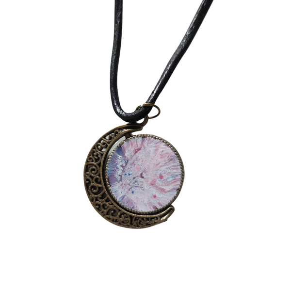 A double-sided moon necklace with one side displaying a pink and blue color resin section and the other side a traditional moon and stars design, attached to a black leather cord.